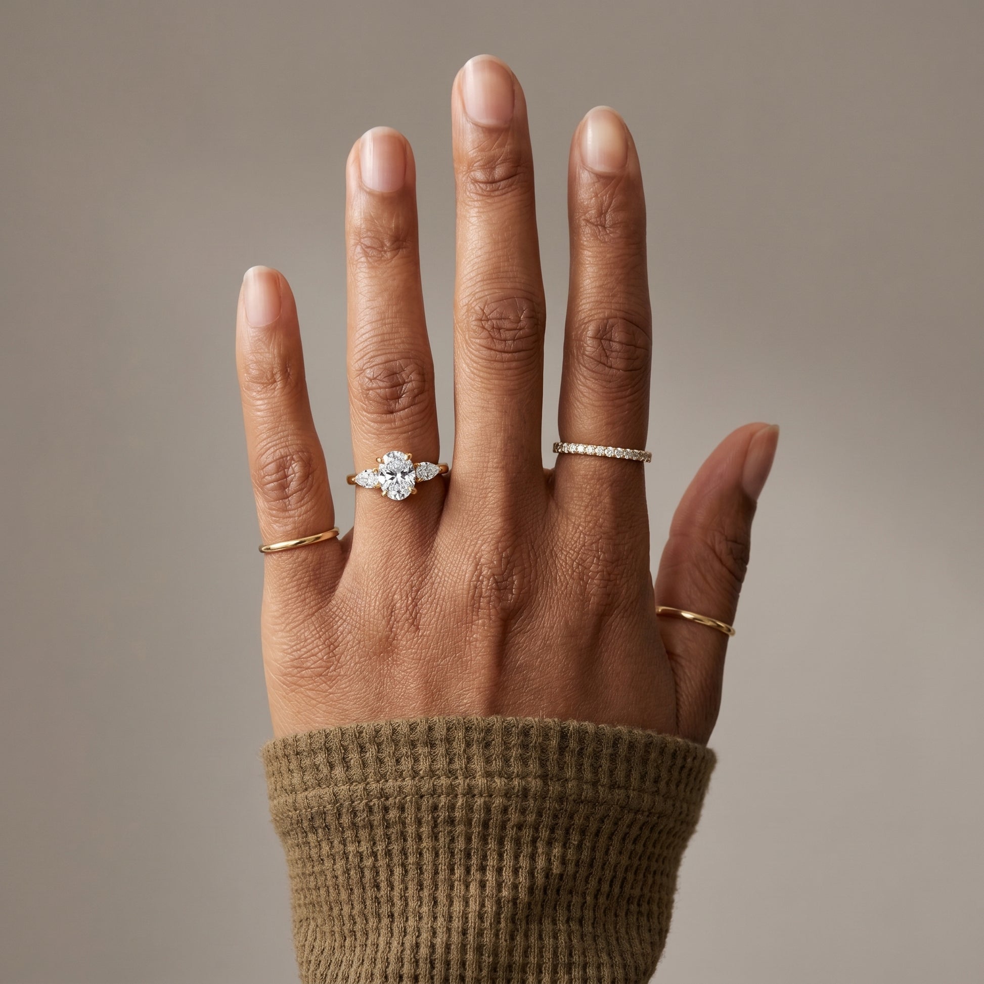 Woman wearing oval moissanite engagement ring with pear side stones in yellow gold plated silver elegant hand shot