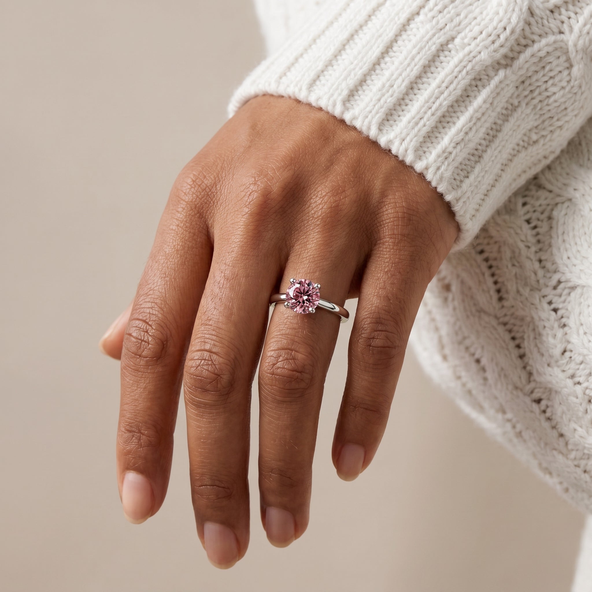 Close up of pink moissanite engagement ring on hand in sterling silver with round brilliant cut stone